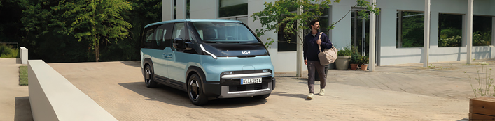 Der Kia PV5 Passenger von vorne rechts vor modernem Familienhaus mit männlichem Model mit Reisetasche